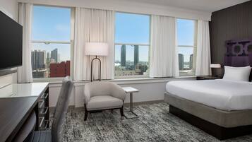 Une chambre d’hôtel dotée d’un grand lit, d’un bureau, d’une chaise, d’une télévision et offrant une vue sur le paysage urbain grâce à de grandes fenêtres.