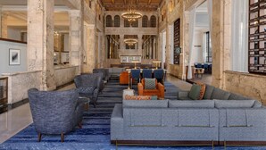 Un vestíbulo espacioso con una imponente escalera, columnas de mármol y un área de descanso con sofás y sillones.