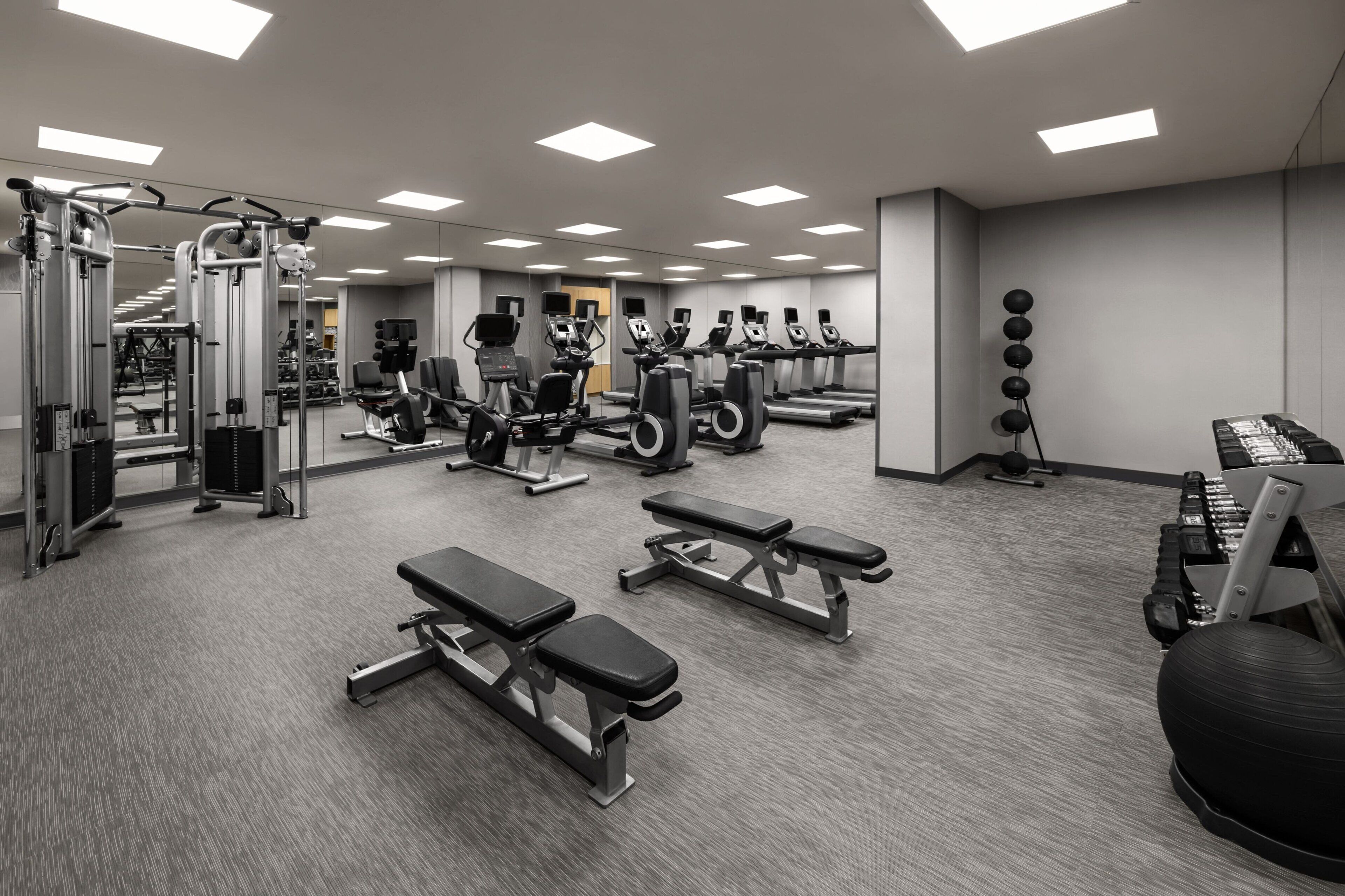 A gym with various exercise equipment, benches, and a mirrored wall.
