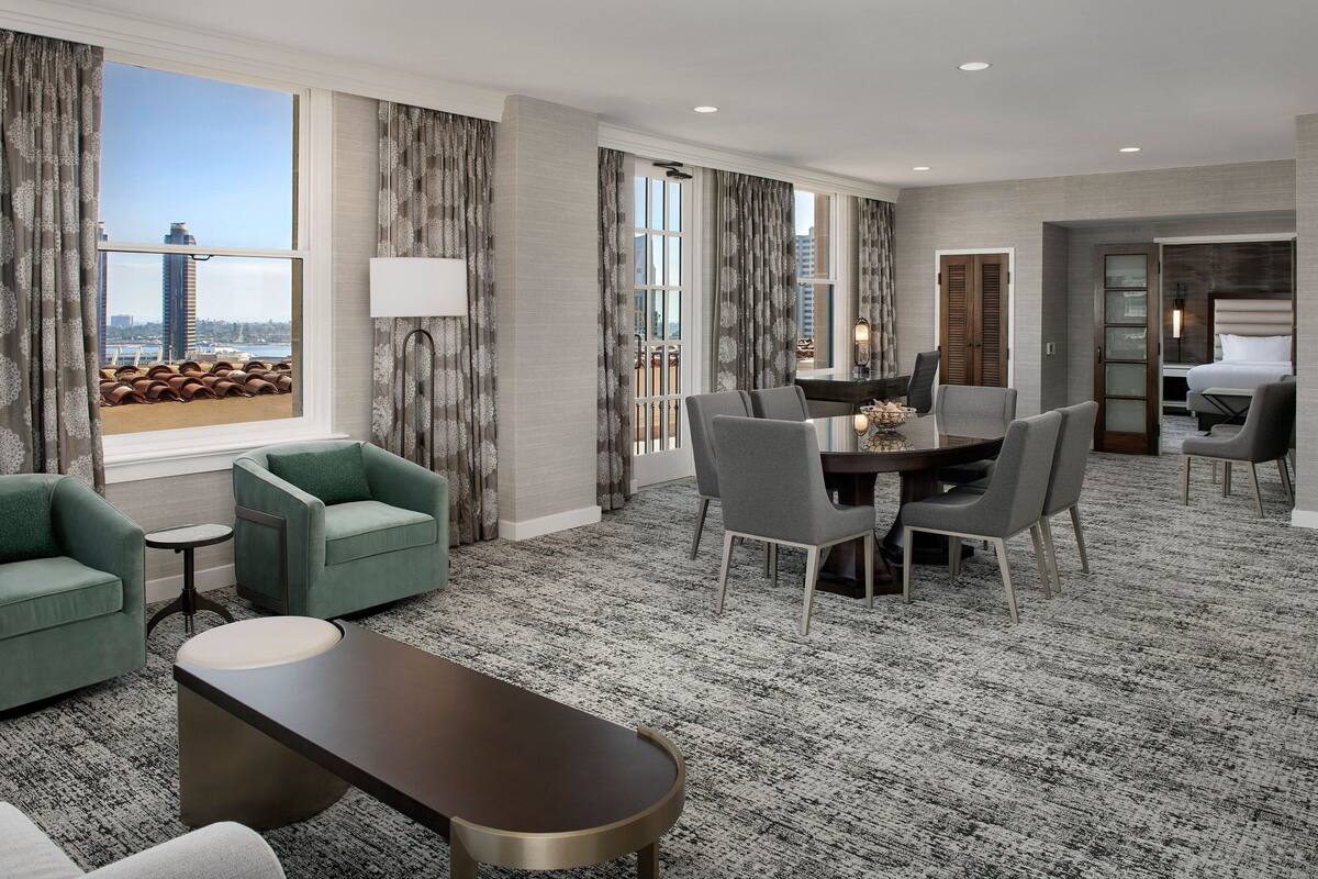 A hotel room with a dining area, a sofa, a coffee table, and a view of the cityscape.
