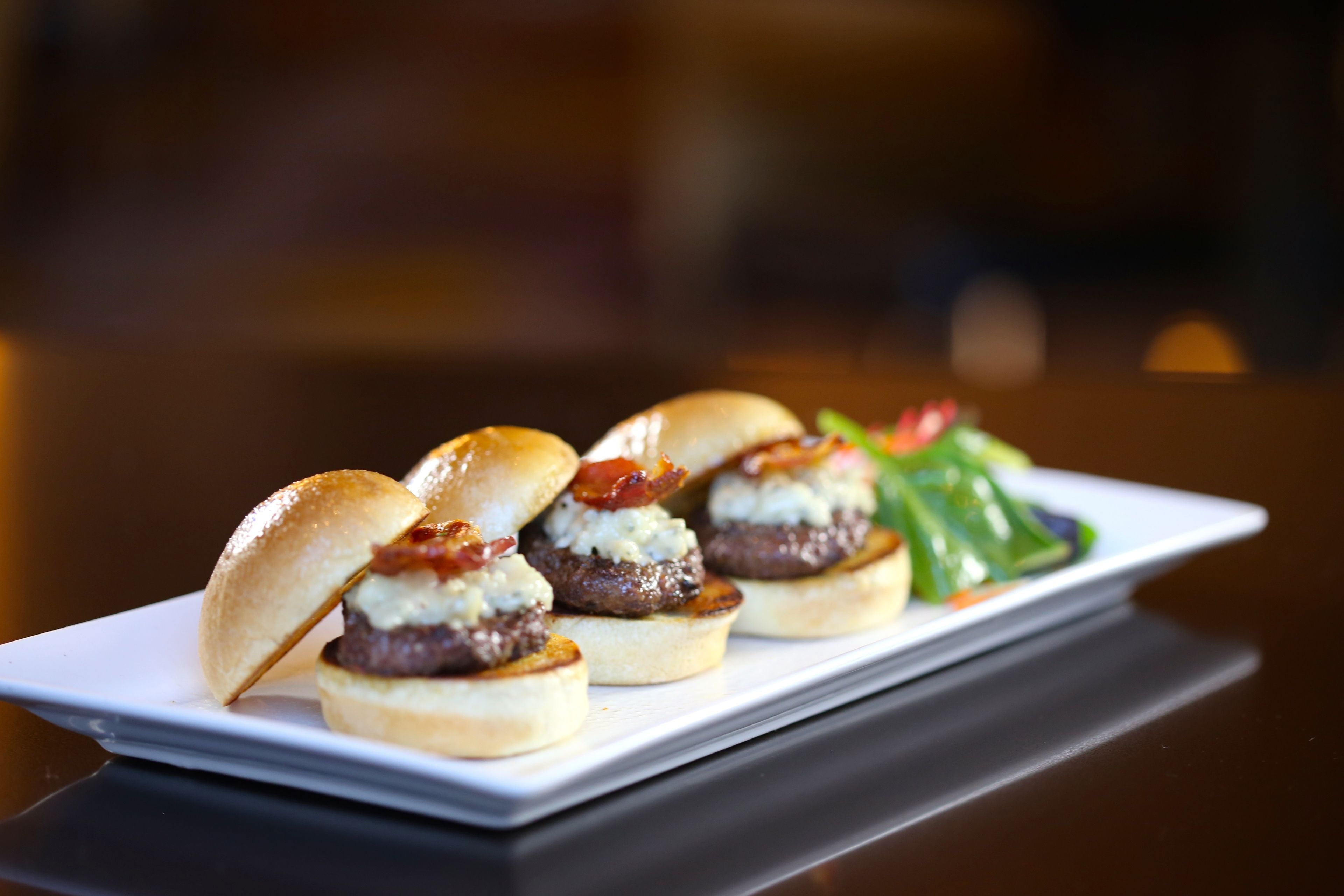 A plate of mini burgers with bacon and cheese, served on a white plate with a side salad.