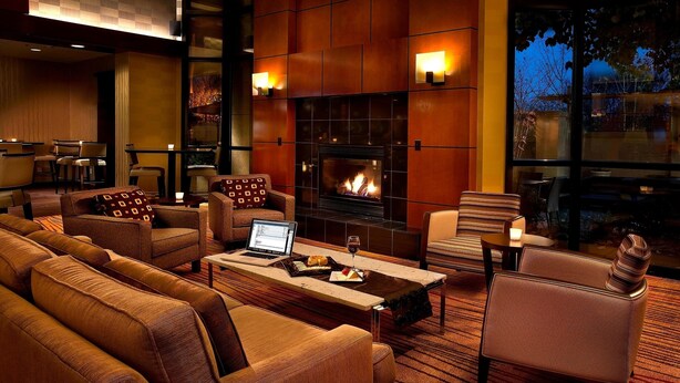 A cozy lounge area with sofas, a fireplace, and a laptop on a table. - Courtyard by Marriott Seattle Sea-Tac Area (Tukwila)