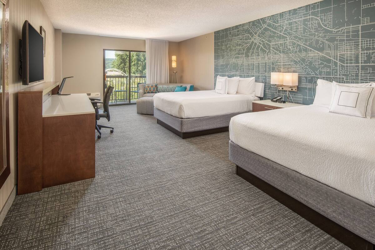 A hotel room with a large bed, a desk, a chair, a TV, and a map on the wall.