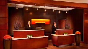 A reception desk with two receptionists, a large vase with orange flowers, and a wall-mounted screen displaying a sunset. - Courtyard by Marriott Seattle Sea-Tac Area (Tukwila)