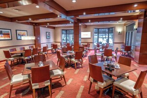 Un salón de conferencias de hotel con varias mesas y sillas, ventanas amplias y una pantalla de proyección.