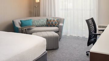 A hotel room with a bed, a sofa, an ottoman, a desk, and a chair.