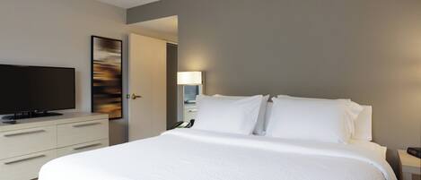 A modern hotel room with a large bed, a flat-screen TV, a bedside table with a lamp, and a painting on the wall.