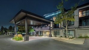 A modern hotel entrance with a covered outdoor area, a sign reading 'COURTYARD BY MARGIE,' and a parking lot. - Courtyard by Marriott Salt Lake City Airport (Salt Lake City)