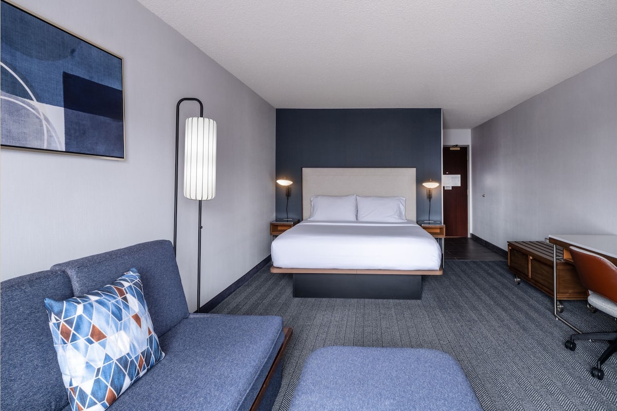 Ein modernes Hotelzimmer mit Bett, Sofa, Schreibtisch und Lampe.