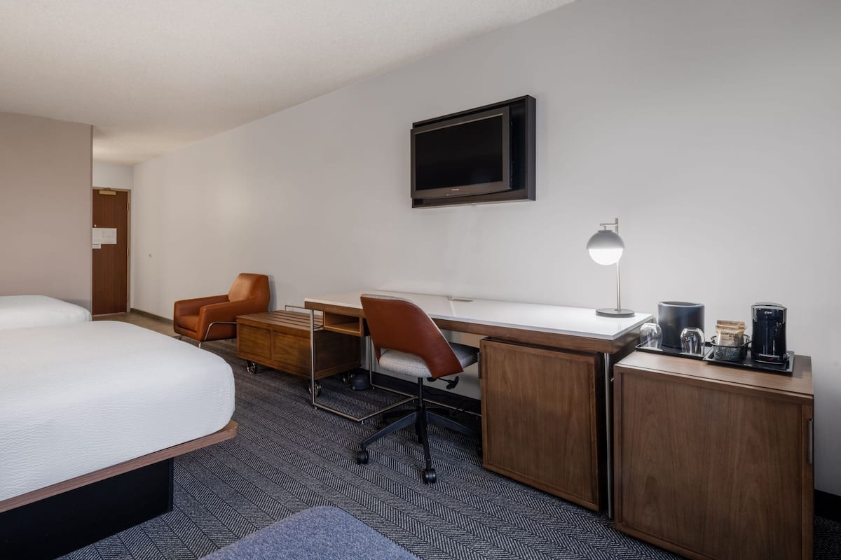 Ein Hotelzimmer mit einem großen Bett, einem Schreibtisch mit Stuhl, einem Fernseher und einer Kaffeemaschine.