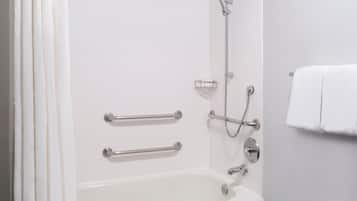Un baño blanco con bañera, barras de apoyo, cabezal de ducha y barra para toallas.