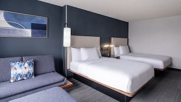A modern hotel room with a grey sofa, a large bed, and a small table.