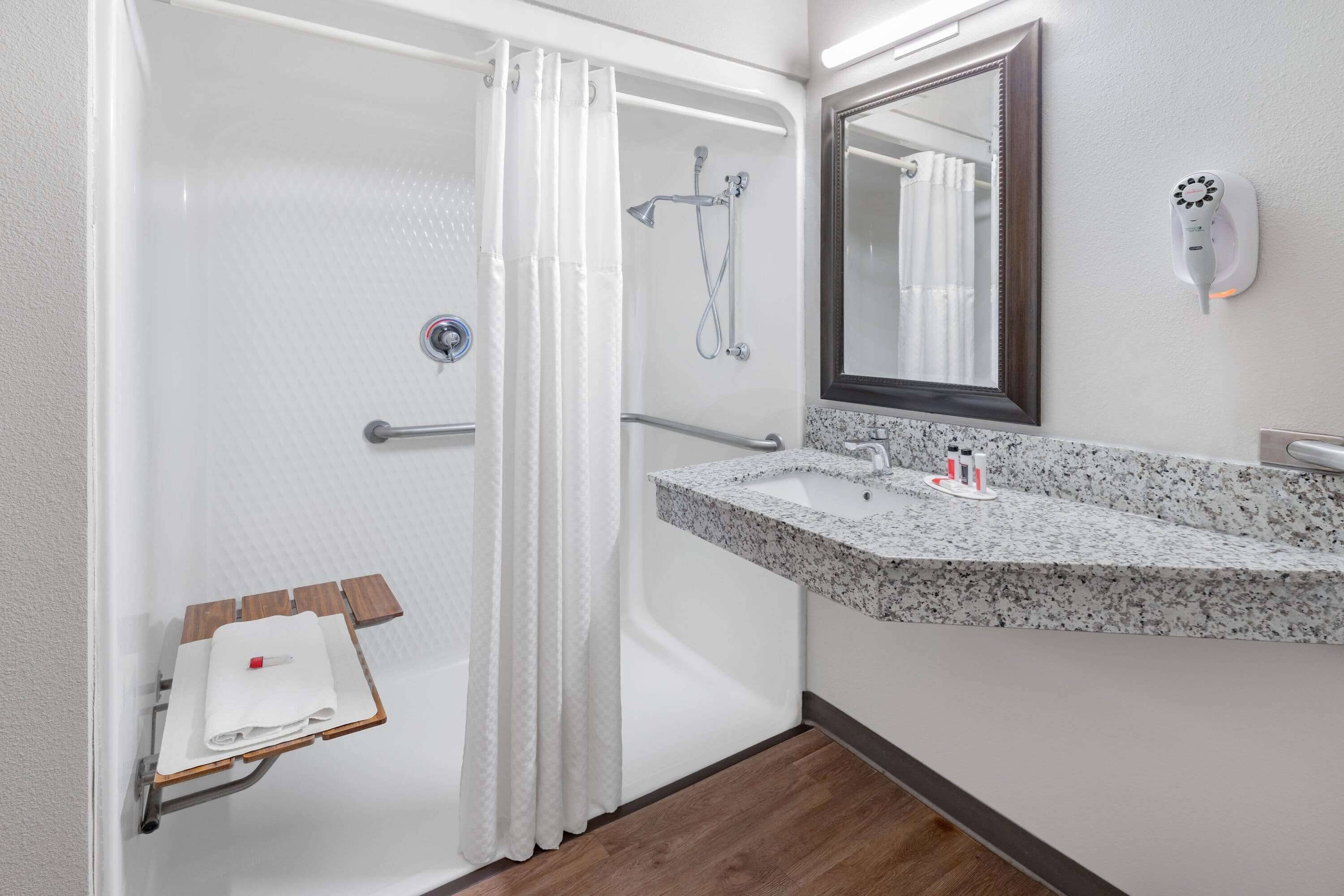 A bathroom with a shower, a sink with a granite countertop, a towel rack, and a mirror.