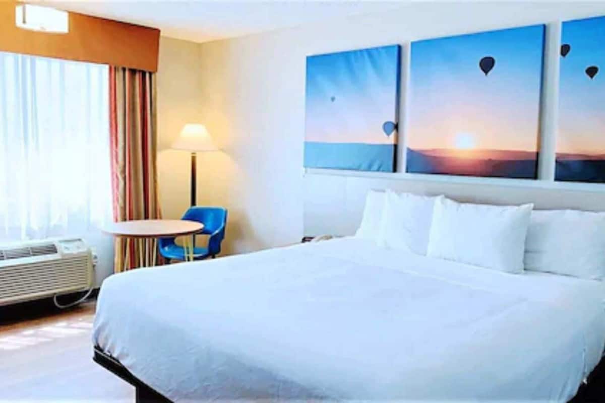 A hotel room with a large bed, a desk, a chair, and a window with curtains.