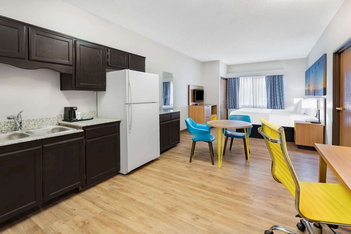 A compact hotel room with a kitchenette, a dining area with two chairs, a bed, and a TV.