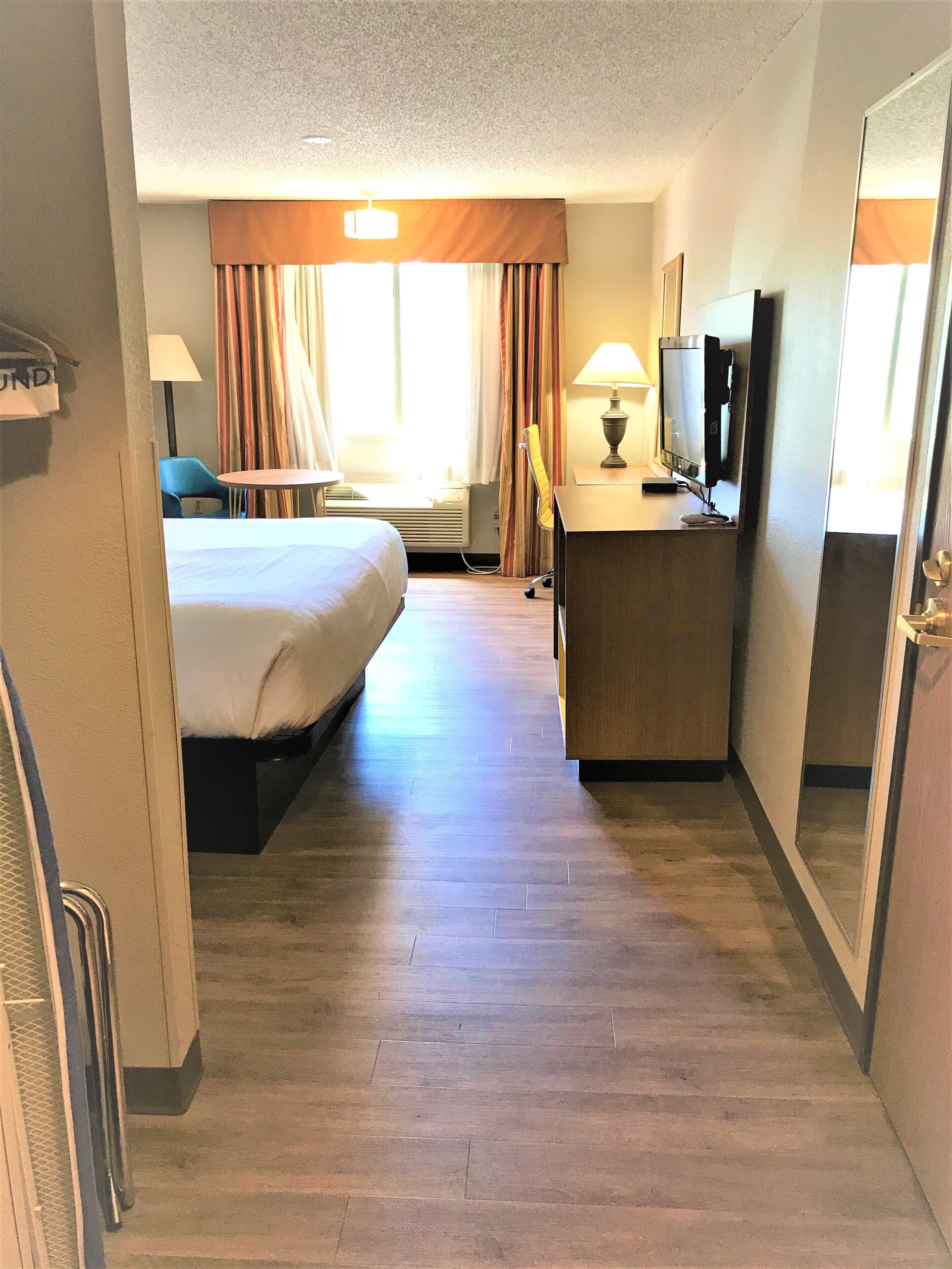A hotel room with a bed, desk, TV, and a large mirror.
