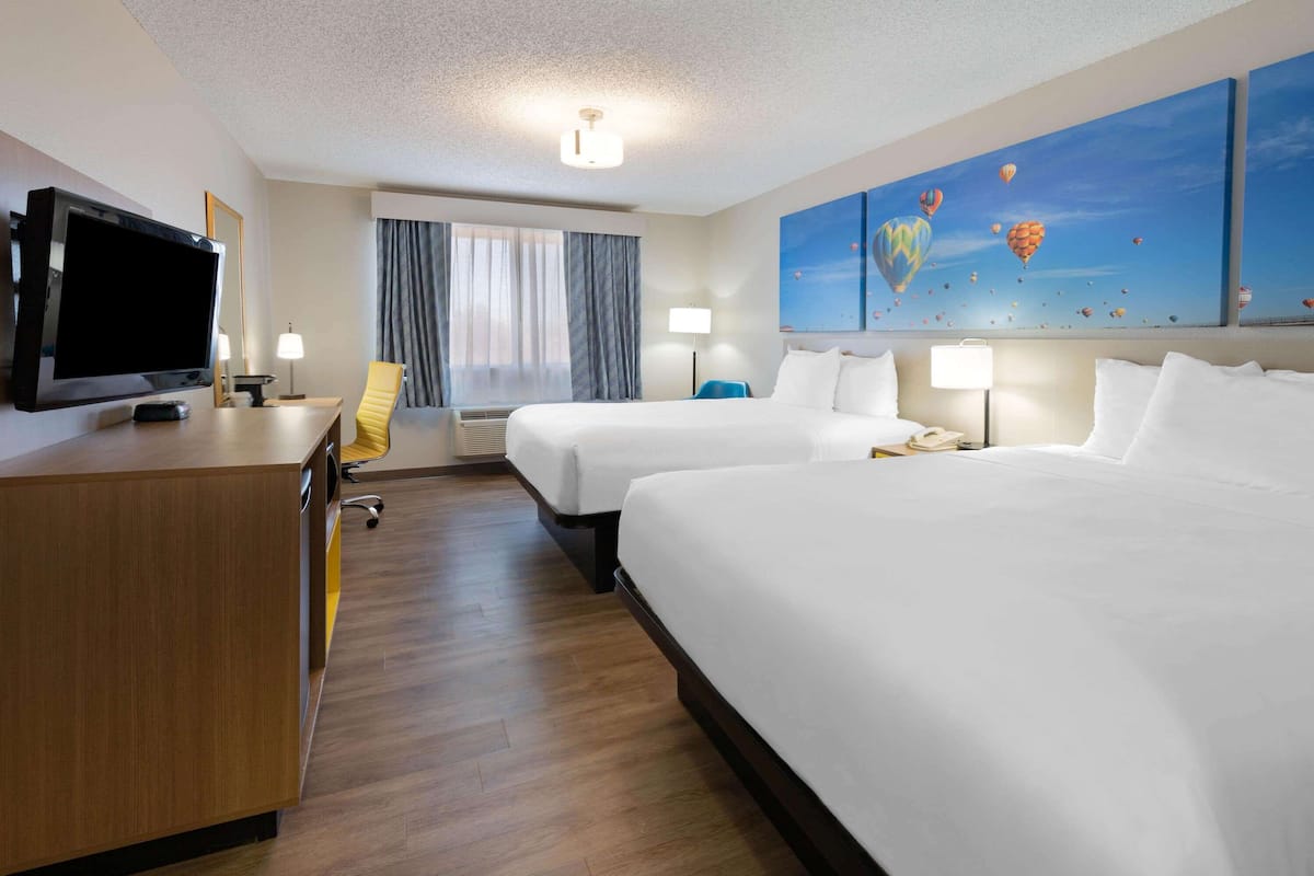 A hotel room with two beds, a desk, a television, and a painting of hot air balloons.