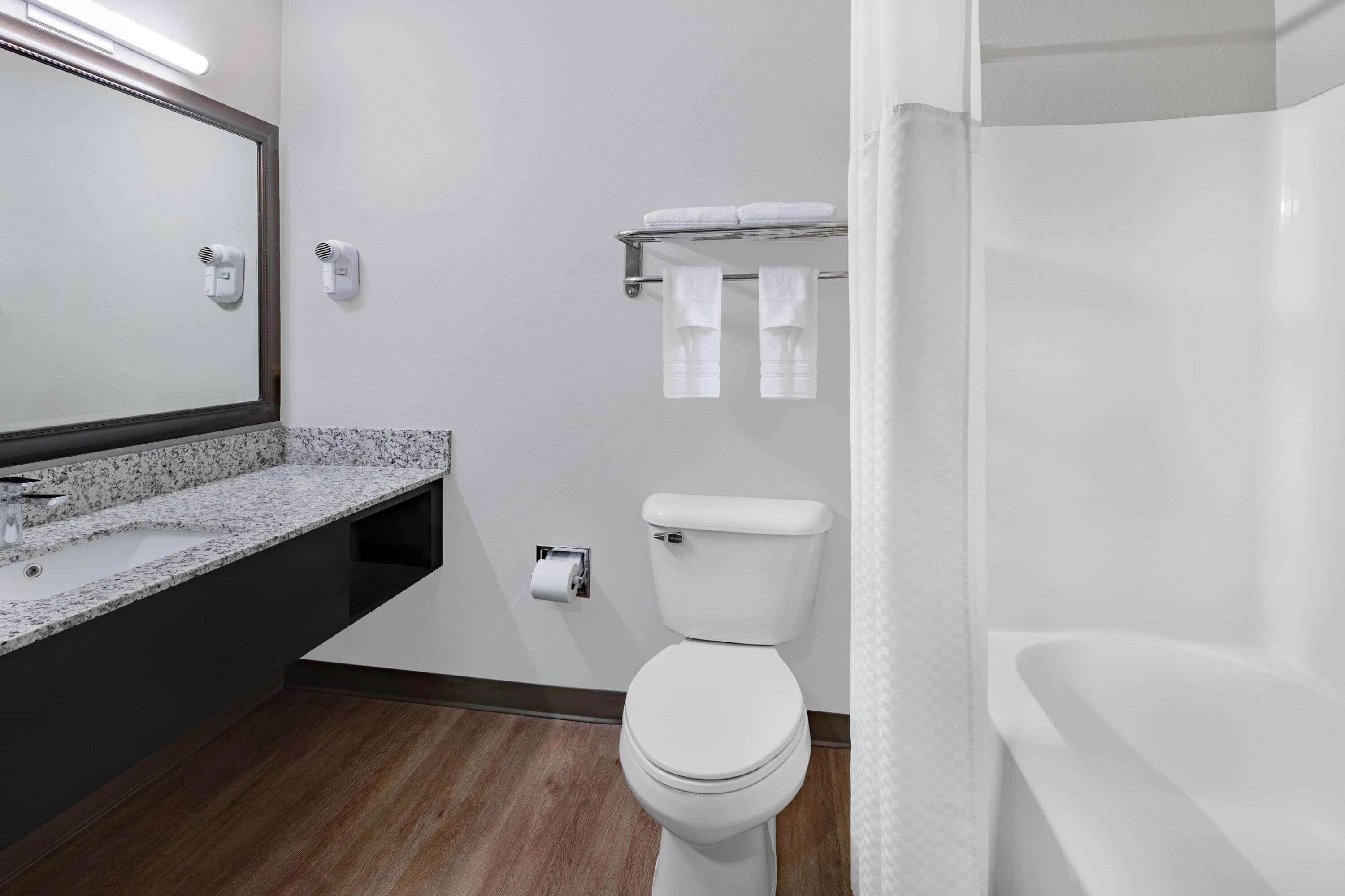 Un baño moderno con inodoro blanco, lavamanos con encimera de granito, toallero con dos toallas y cortina de ducha.
