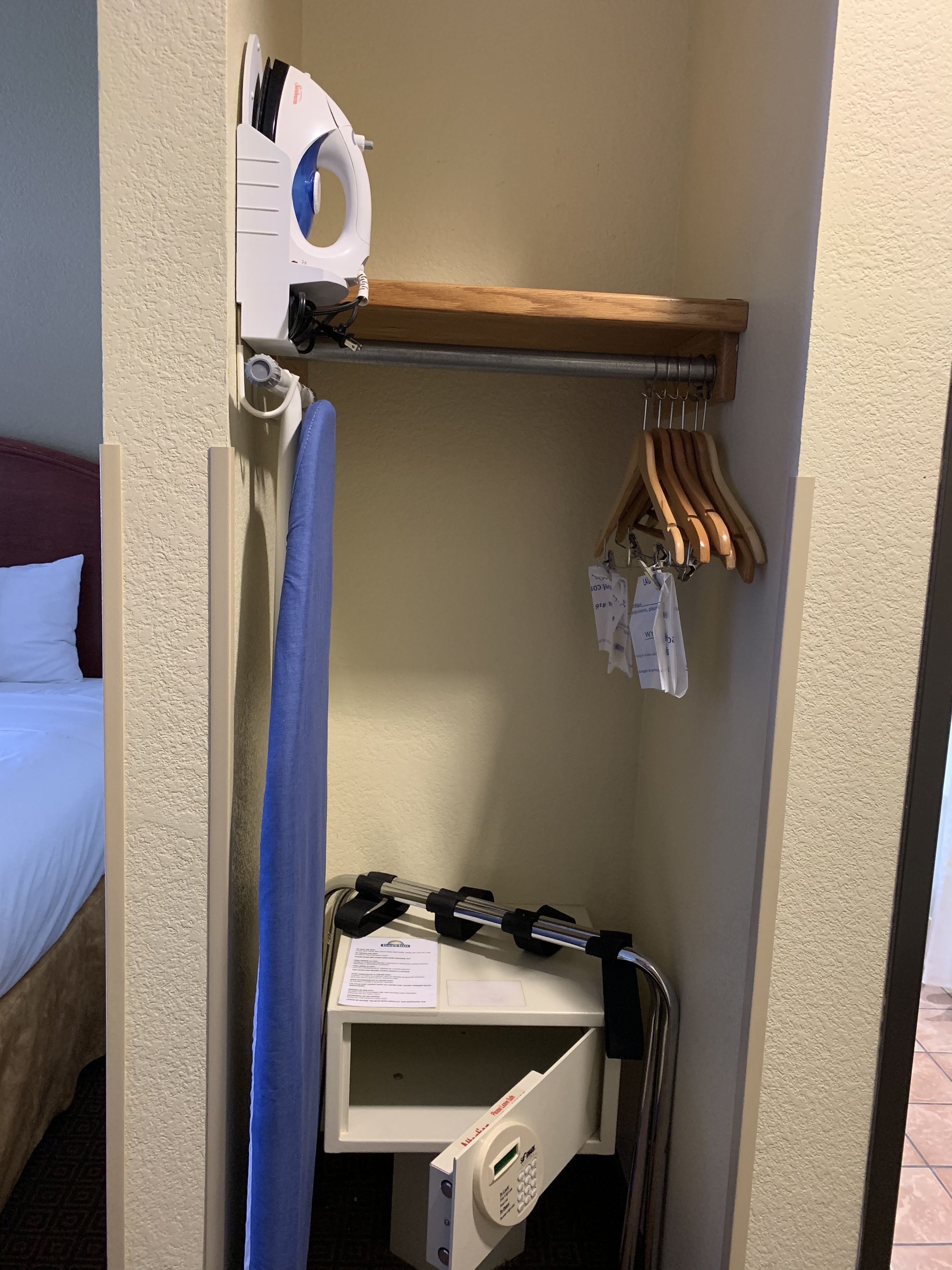 A hotel room with a bed, a small desk with a computer, a hanging clothes rack, and a shower curtain.