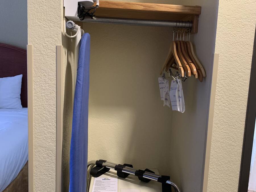 A hotel room with a bed, a small desk with a computer, a hanging clothes rack, and a shower curtain.