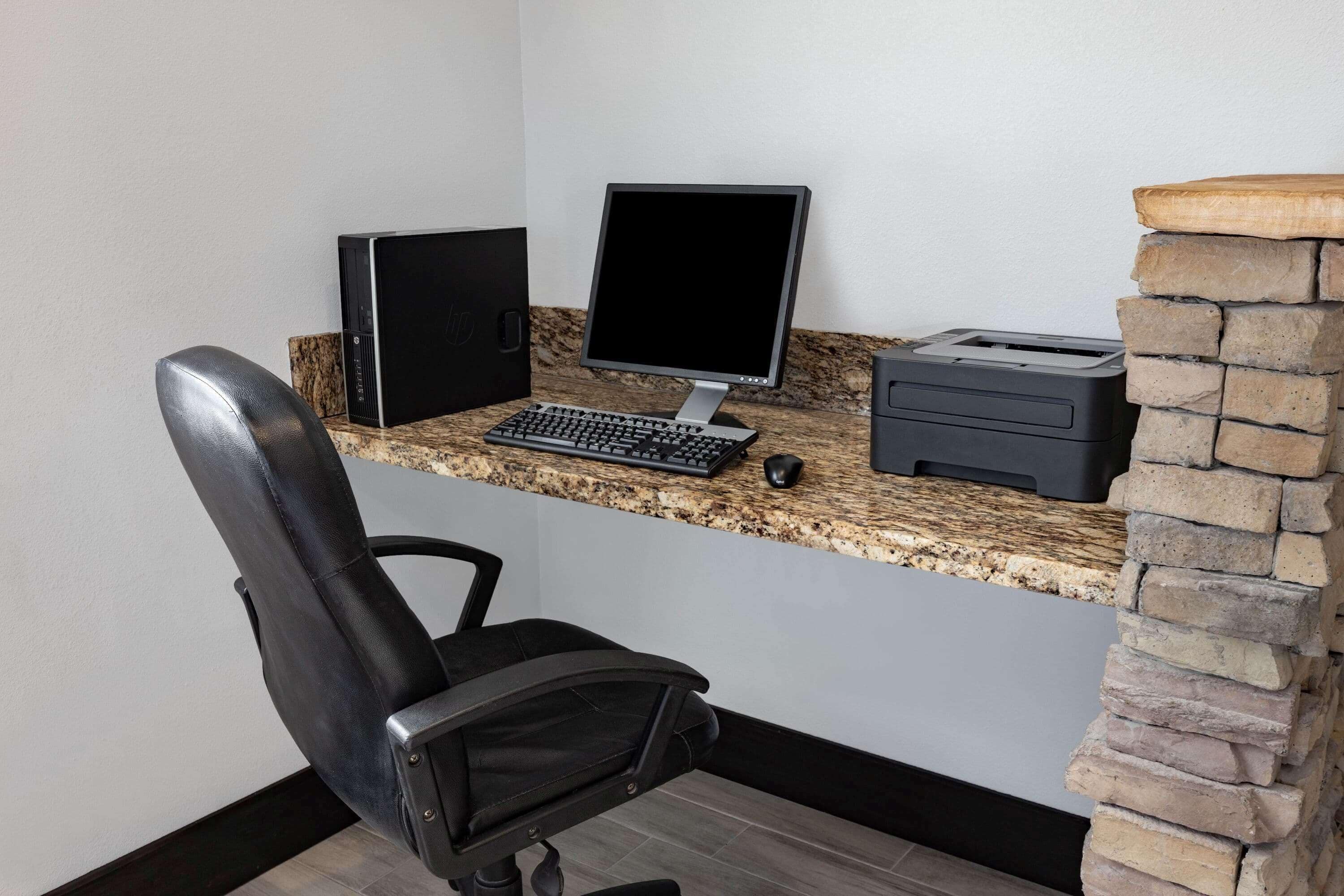 Un espacio de oficina en casa con una computadora de escritorio, teclado, ratón e impresora sobre una encimera de granito.