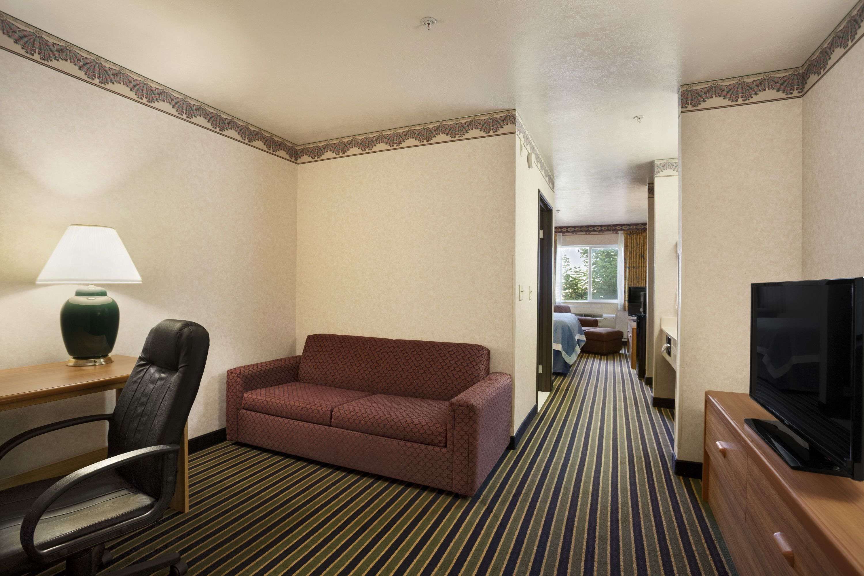 A hotel room with a sofa, a desk with a lamp, a television, and a striped carpet.