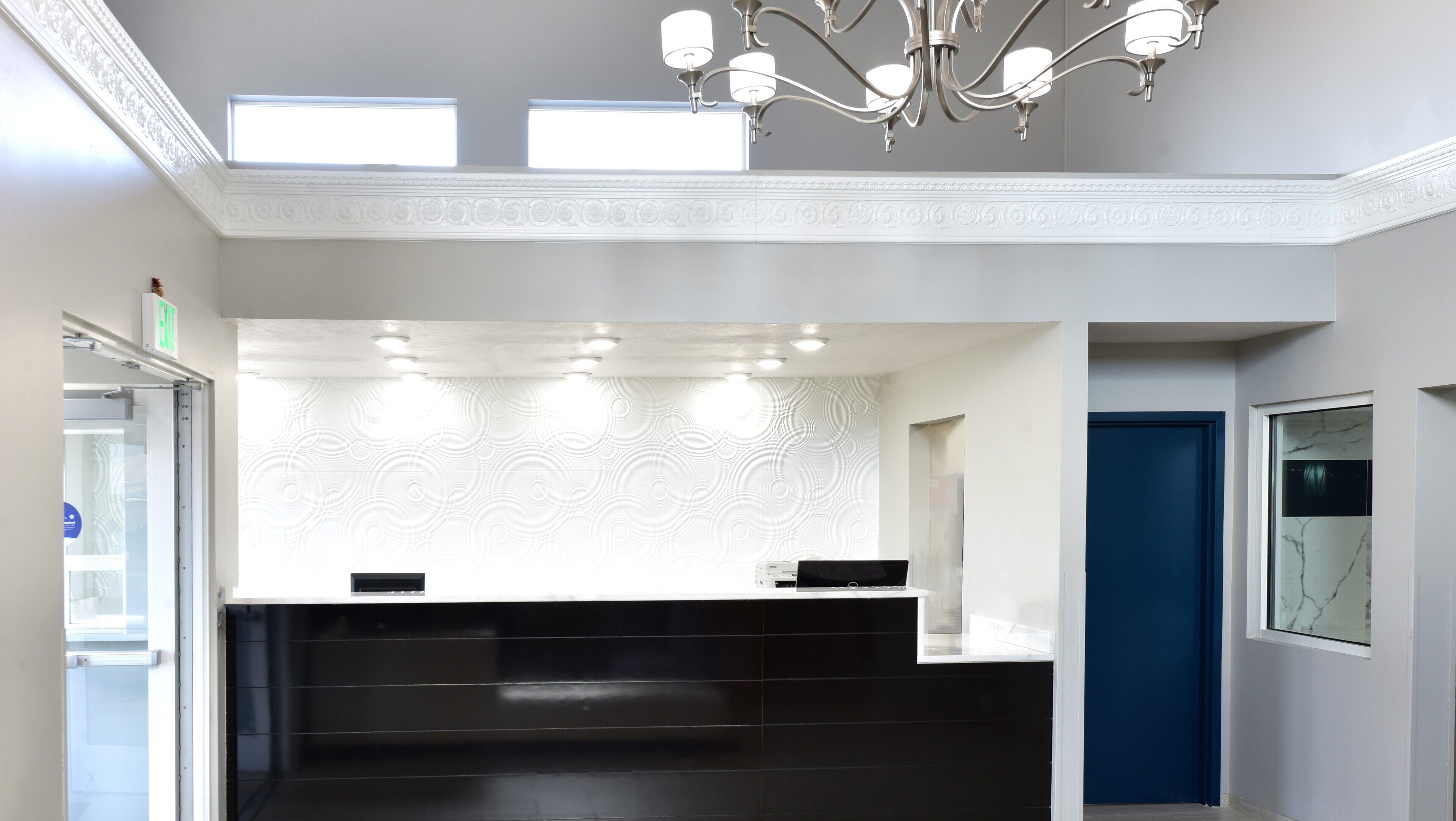 A reception area with a black counter, white patterned wall, and a chandelier.