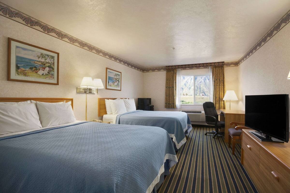 A hotel room with two beds, a desk with a TV, a chair, and a window with curtains.