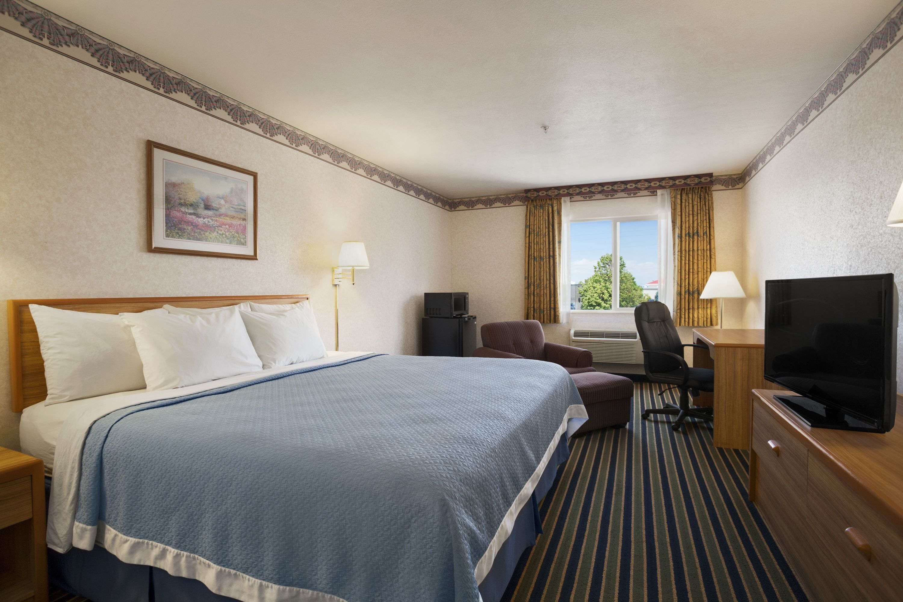 A hotel room with a bed, a desk with a chair, a television, and a window with curtains.