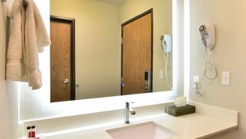 A bathroom with a large mirror, a sink, a towel rack, a hairdryer, and a soap dispenser.