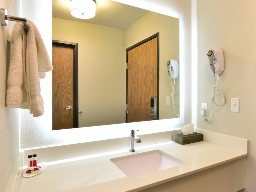 A bathroom with a large mirror, a sink, a towel rack, a hairdryer, and a soap dispenser.