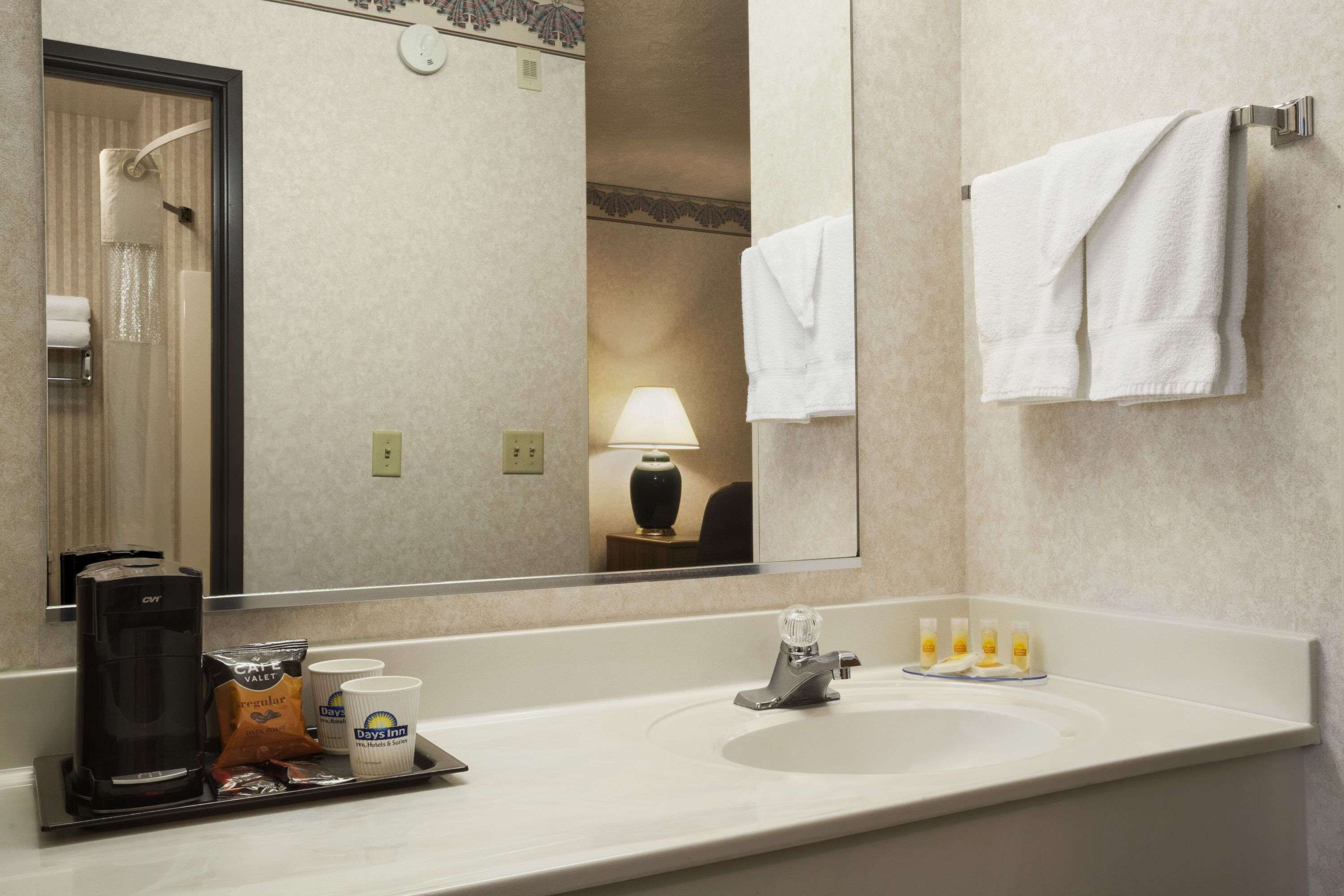 Un baño de hotel con un espejo grande, un lavamanos, una cafetera y artículos de tocador.