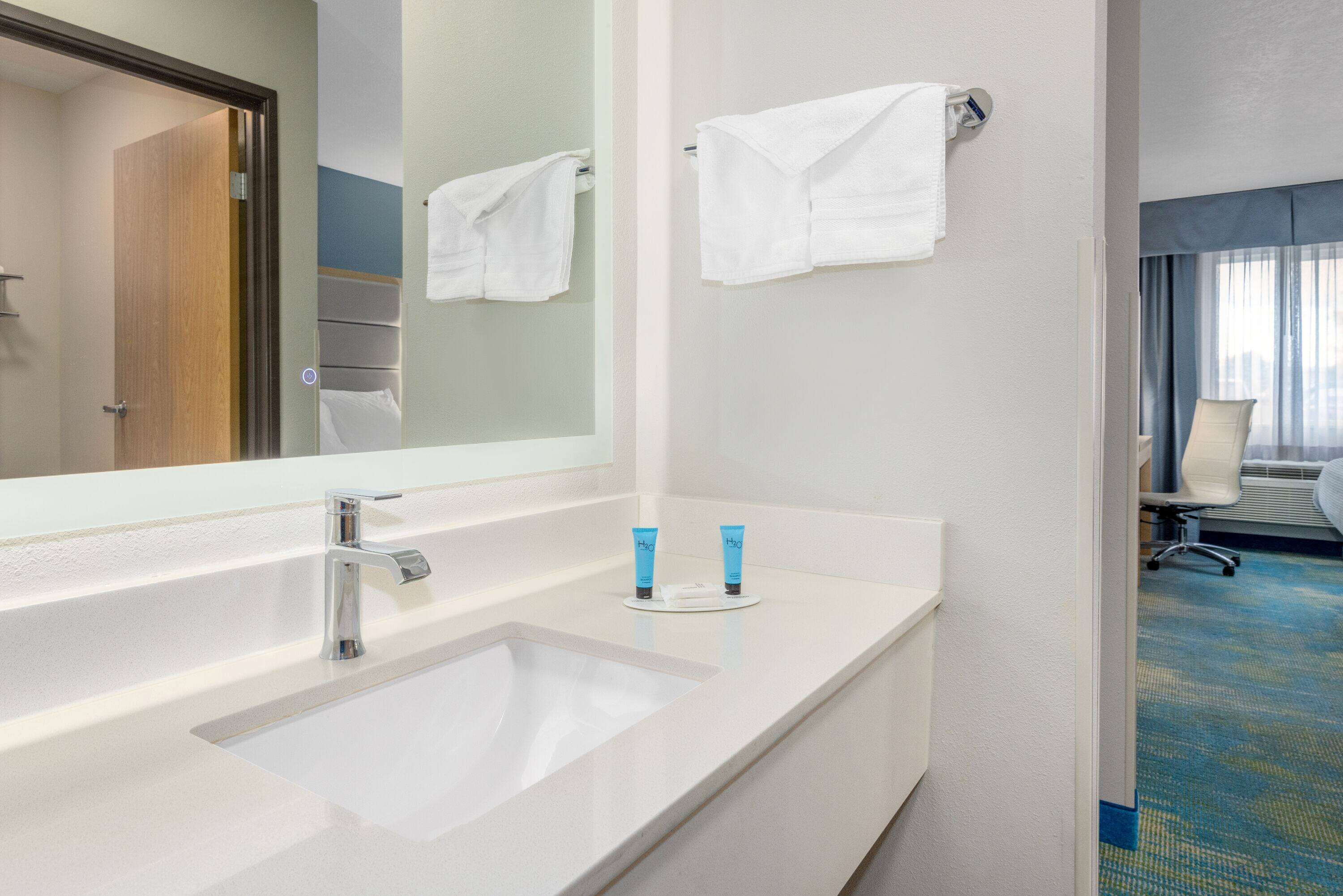 Un baño de hotel con un espejo grande, un lavabo blanco y dos artículos de tocador en la encimera.