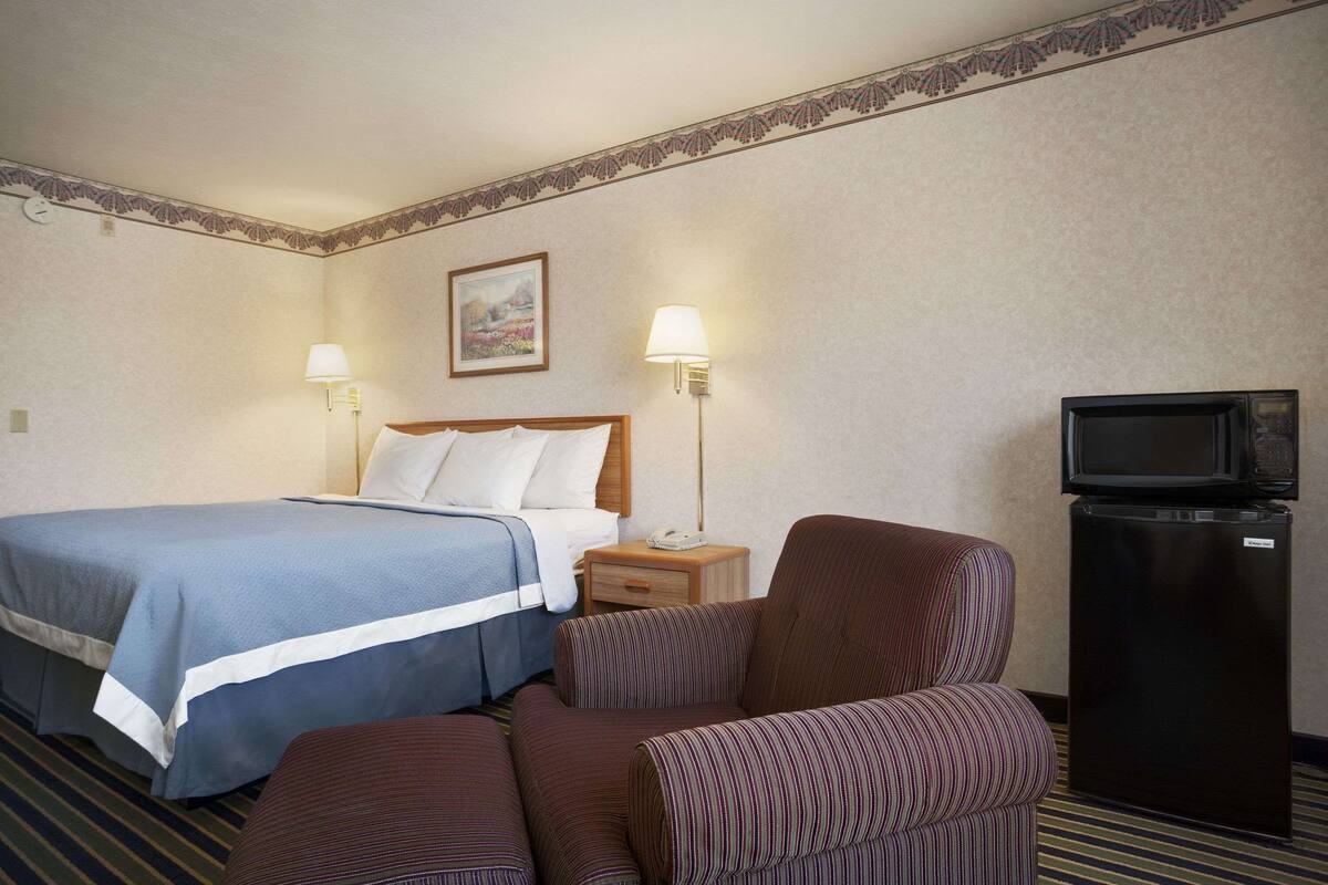 A hotel room with a bed, two bedside lamps, a television, and a small refrigerator.