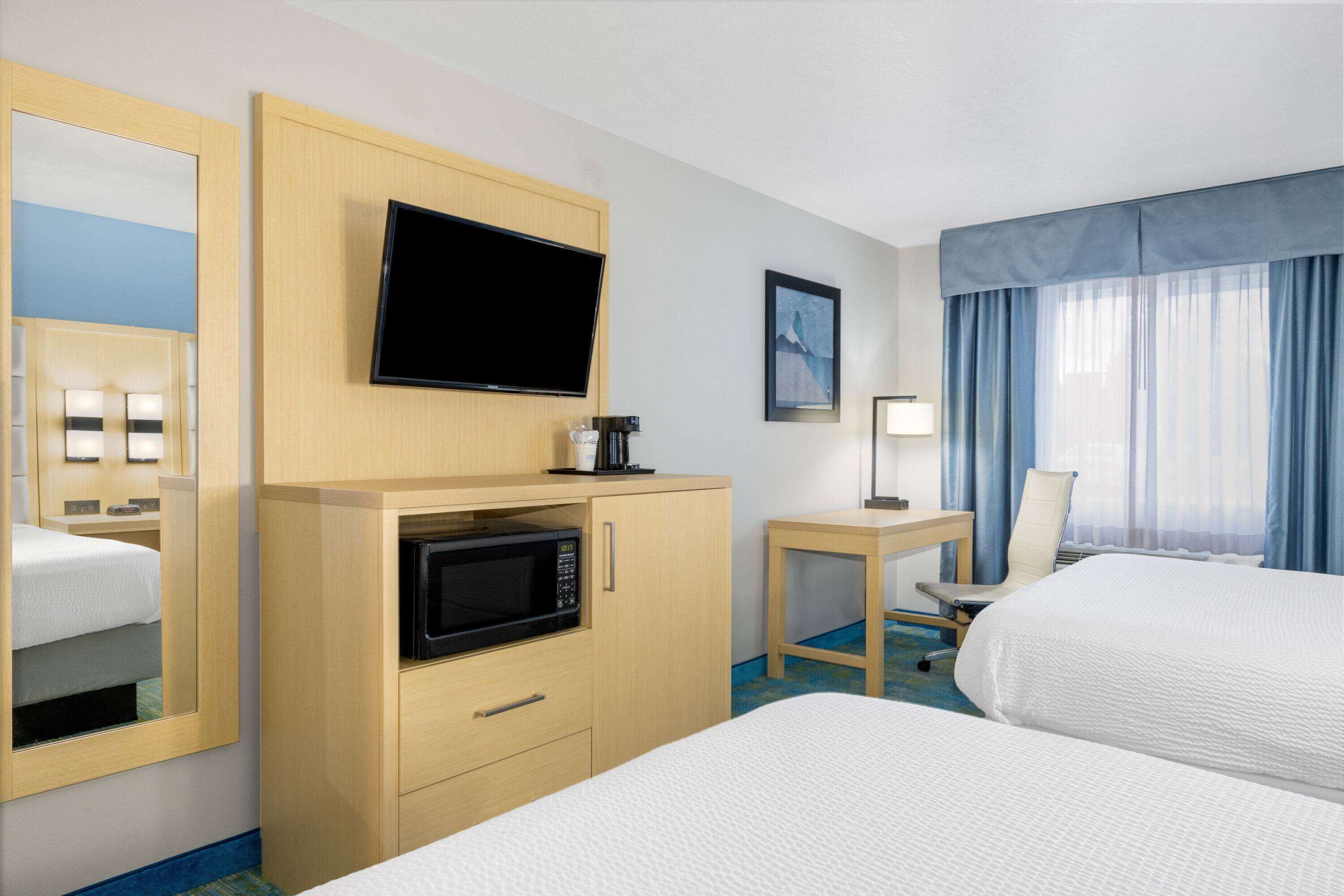 Een hotelkamer met een bed, een bureau met stoel, een televisie, een magnetron en een raam met gordijnen.