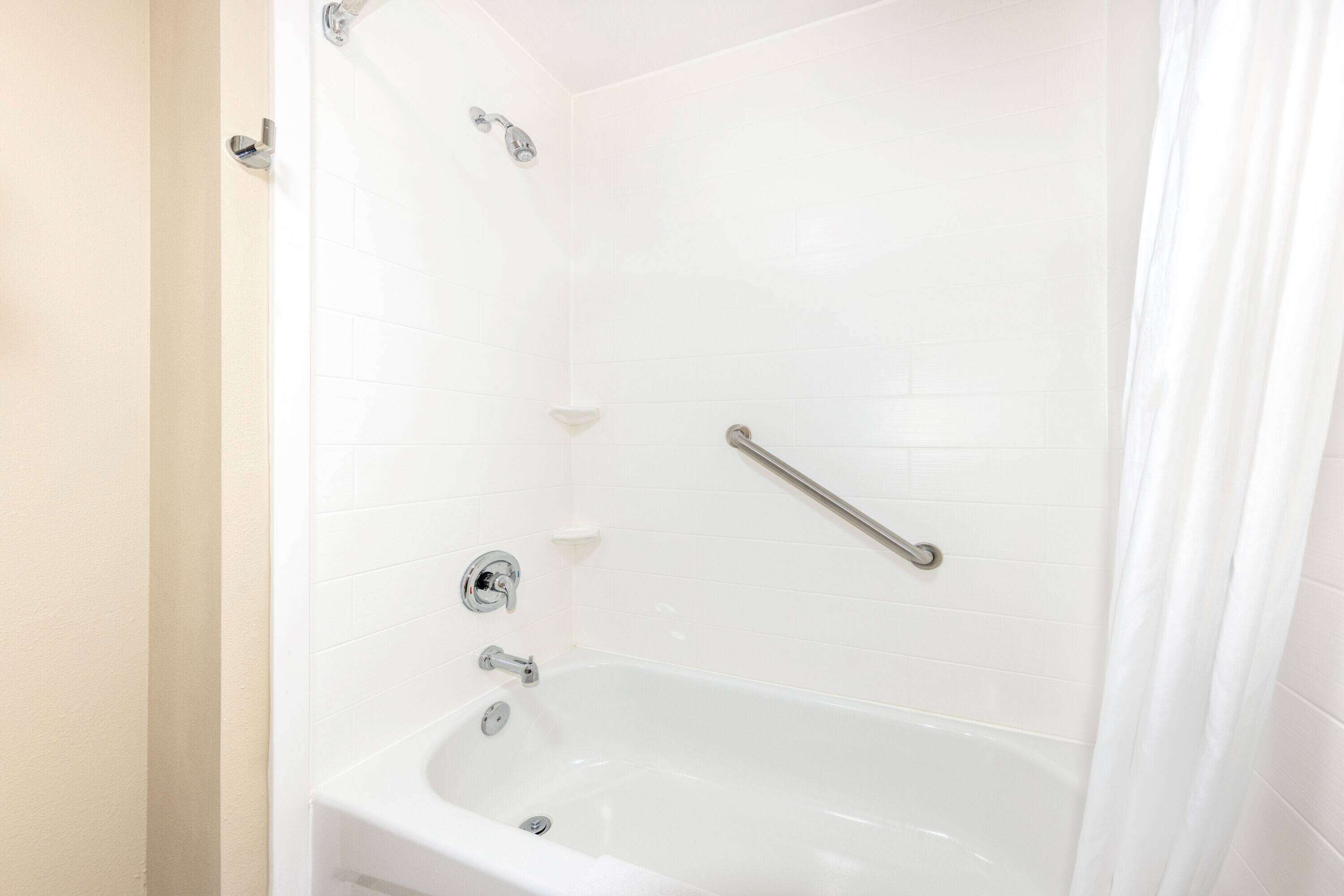 A white bathtub with chrome fixtures, a handheld showerhead, and a grab bar.