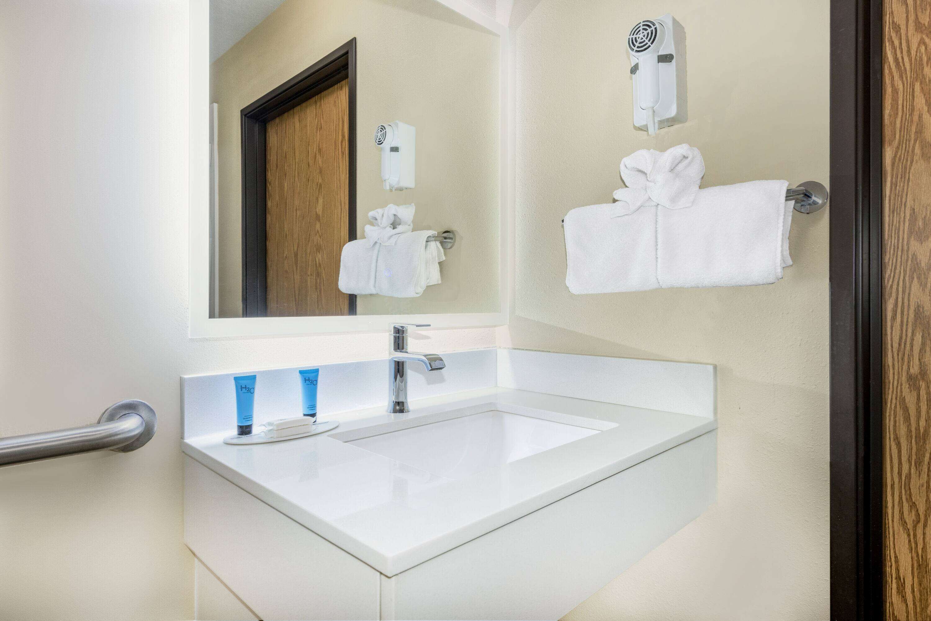 A bathroom with a white sink, a mirror, a towel rack with towels, and a hair dryer on the wall.