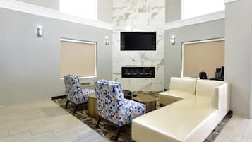 A modern living room with a flat-screen TV, a fireplace, a ceiling fan, and a large window.