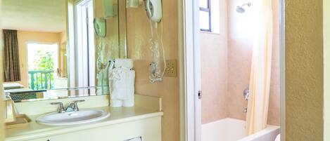 A bathroom with a sink, mirror, towel rack, and a shower area.