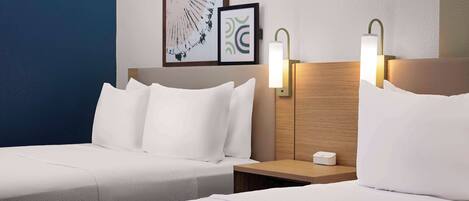 A hotel room with two beds, a wooden headboard, a nightstand with a lamp, and framed artwork on the wall.