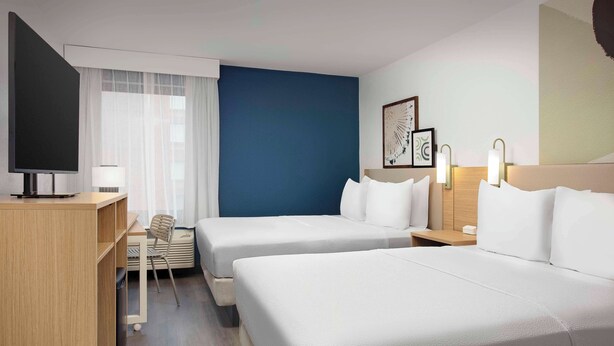 Habitación de hotel con dos camas, un escritorio, una silla, un televisor y una ventana con cortinas.