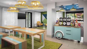 Un café moderno con mesas de madera, luces colgantes amarillas y una estación de café con diversas opciones de bebidas.