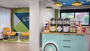 Un área de estar moderna con una barra de color turquesa, una estación de café con varios dispensadores y asientos cómodos.