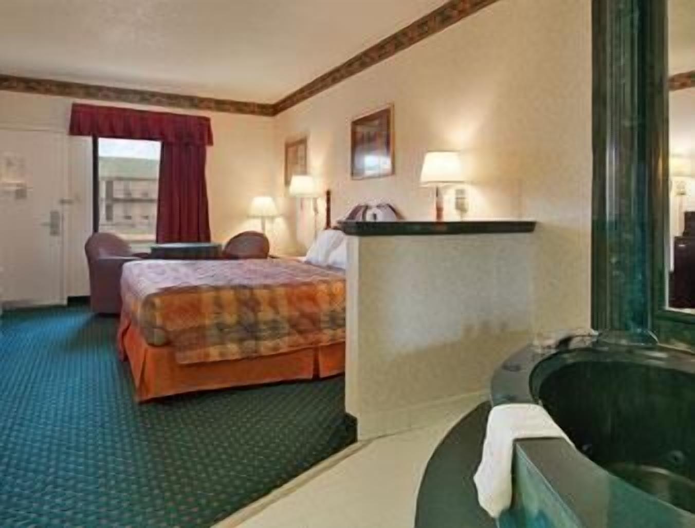 Una habitación de hotel con cama, escritorio, silla, lámpara de escritorio, mesita de noche, espejo y bañera.