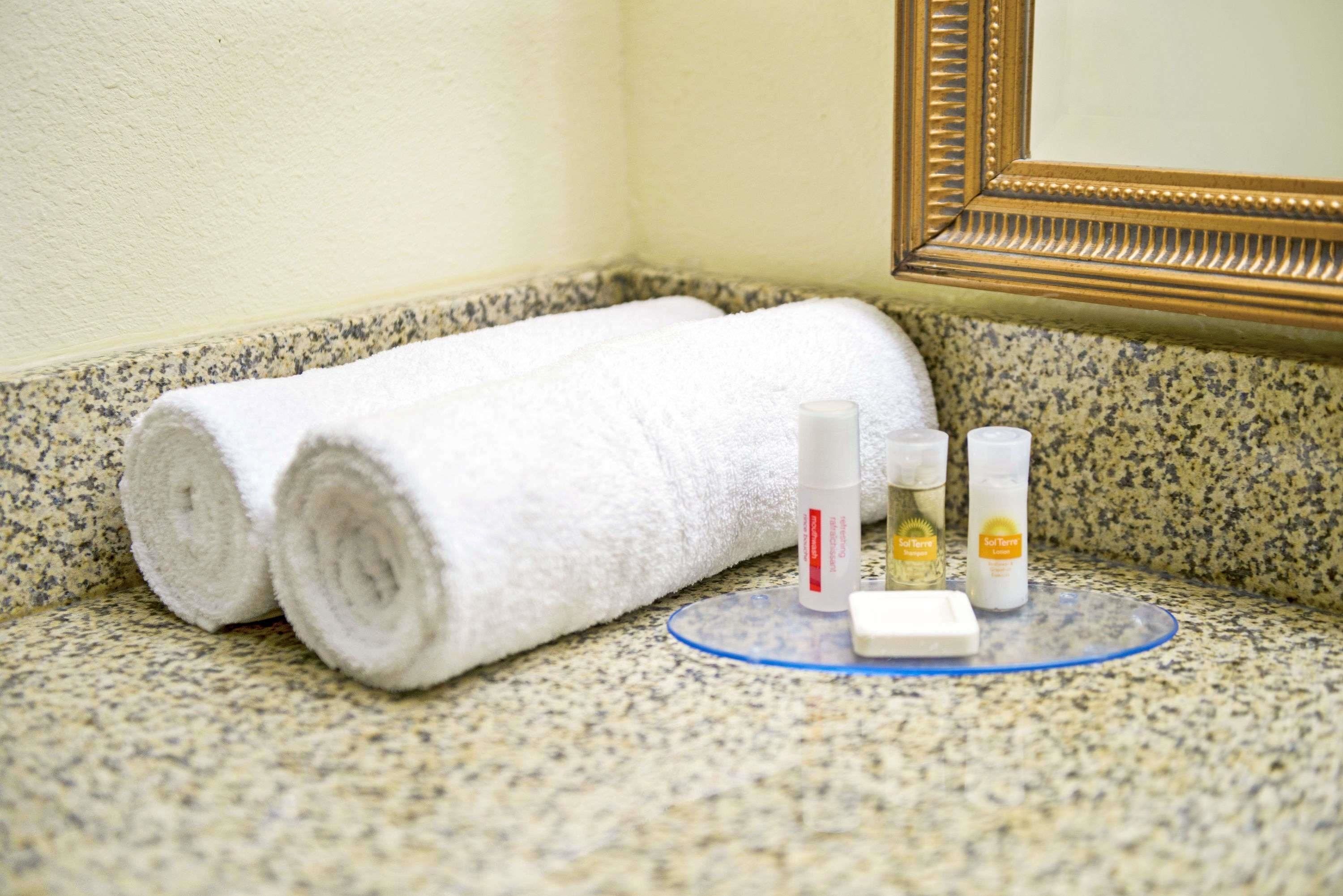 Una encimera de baño con dos toallas enrolladas, un dispensador de jabón y una botella de loción.
