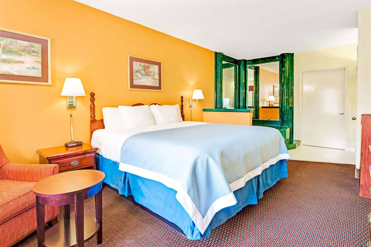 A hotel room with a large bed, two bedside tables with lamps, a chair, a desk, and a mirror.