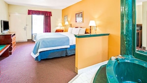 Una habitación de hotel con una cama, un escritorio con computadora, televisión, baño con bañera y ventana con cortinas.