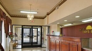 Un vestíbulo de hotel con una recepción, una araña de cristal, piso de baldosas y una puerta que da al exterior.