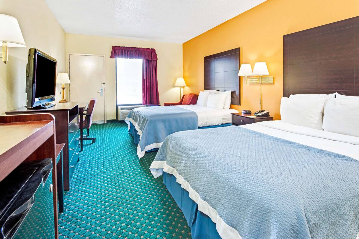 A hotel room with two beds, a desk with a computer, a TV, and a window with curtains.