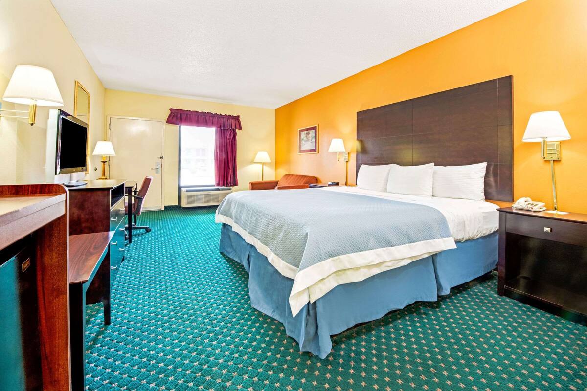 A hotel room with a large bed, a desk, a chair, a television, and a window with curtains.